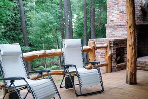 A wooden deck with two white chairs and a brick fireplace.