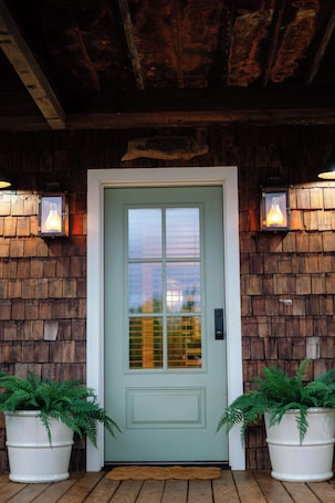 A wooden exterior with a green door, two potted ferns, and wall-mounted lanterns.. The Springs•Luxury 4BR Cabin Retreat on a Natural Spring, pet-friendly!