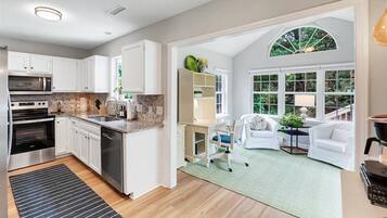 A modern kitchen with built-in appliances, a dining area with a white table and chairs, and a large window with a view of greenery.