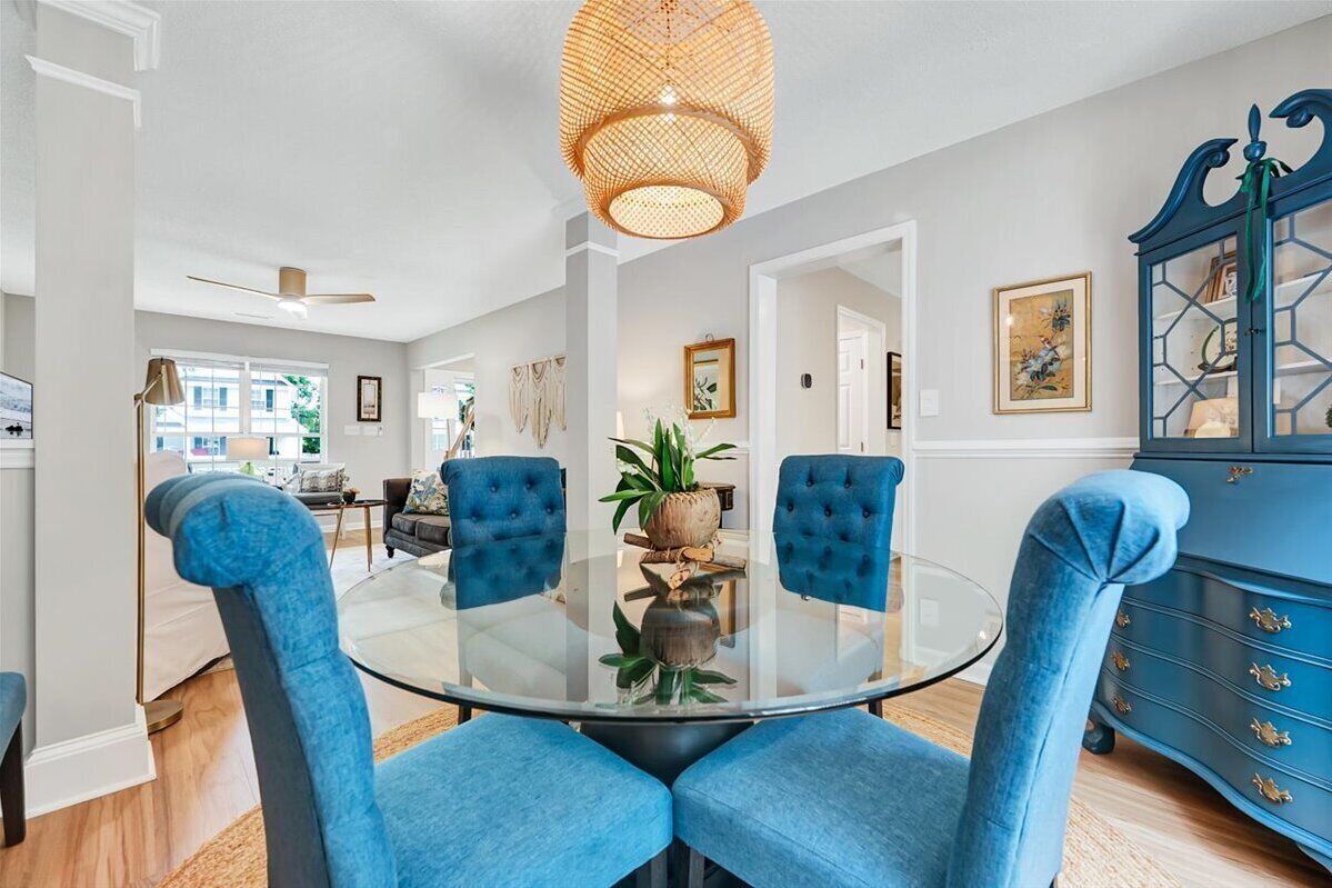 A dining area with a glass table, blue upholstered chairs, a wicker chandelier, and a blue cabinet with glass doors.