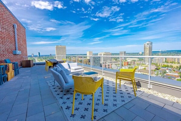 A rooftop terrace with outdoor seating, a brick wall, and a city view.