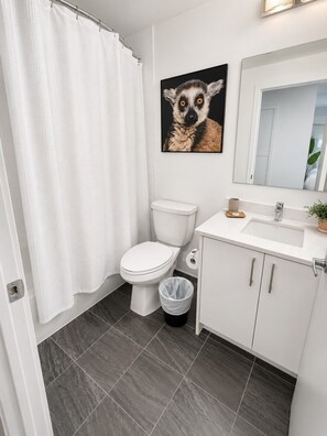 Ein Badezimmer mit Toilette, einer Duschvorhang, einem Waschbecken mit Spiegel und einem Mülleimer.