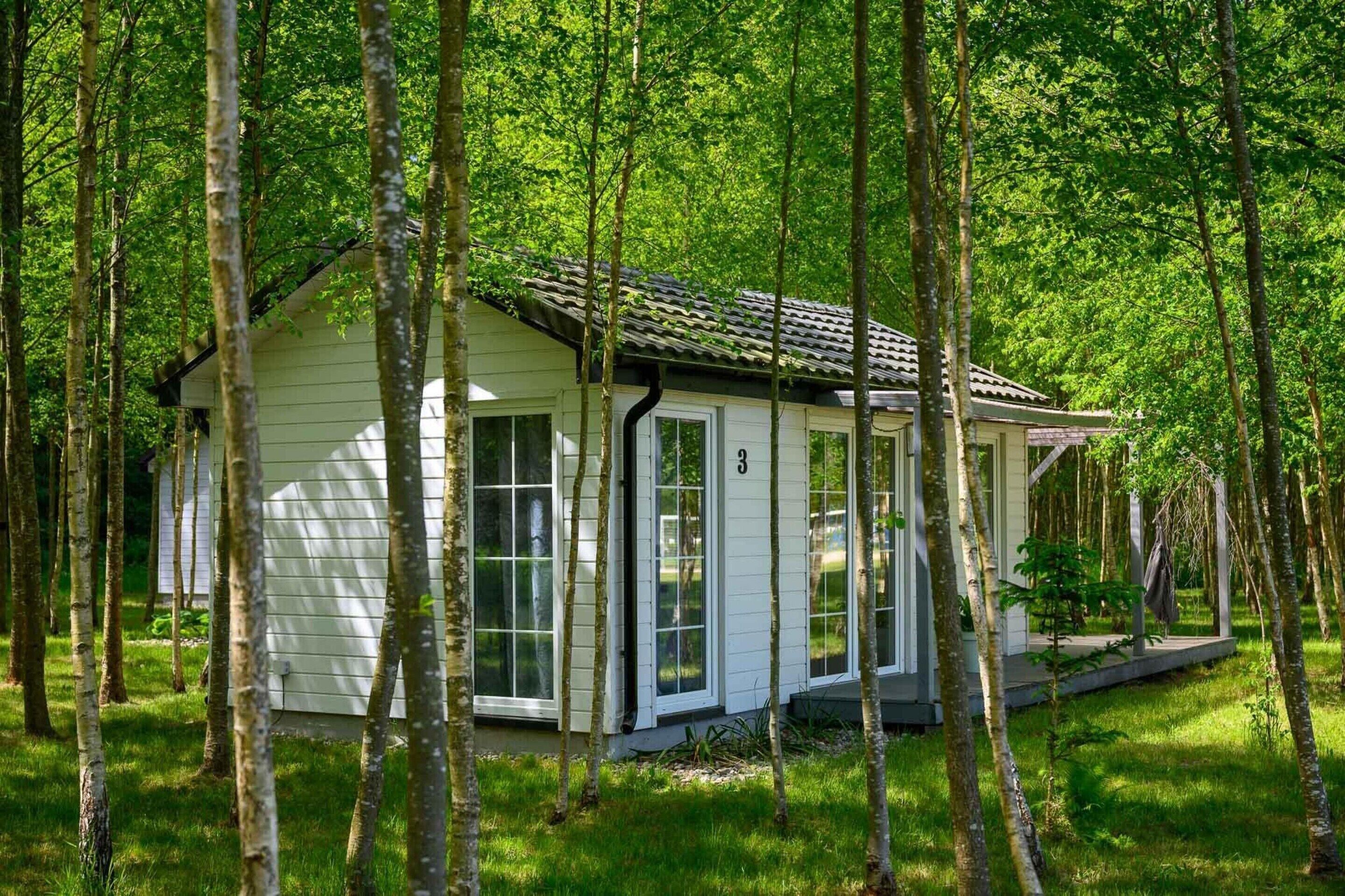 A small, single-story cabin with a gabled roof, surrounded by a forested area.