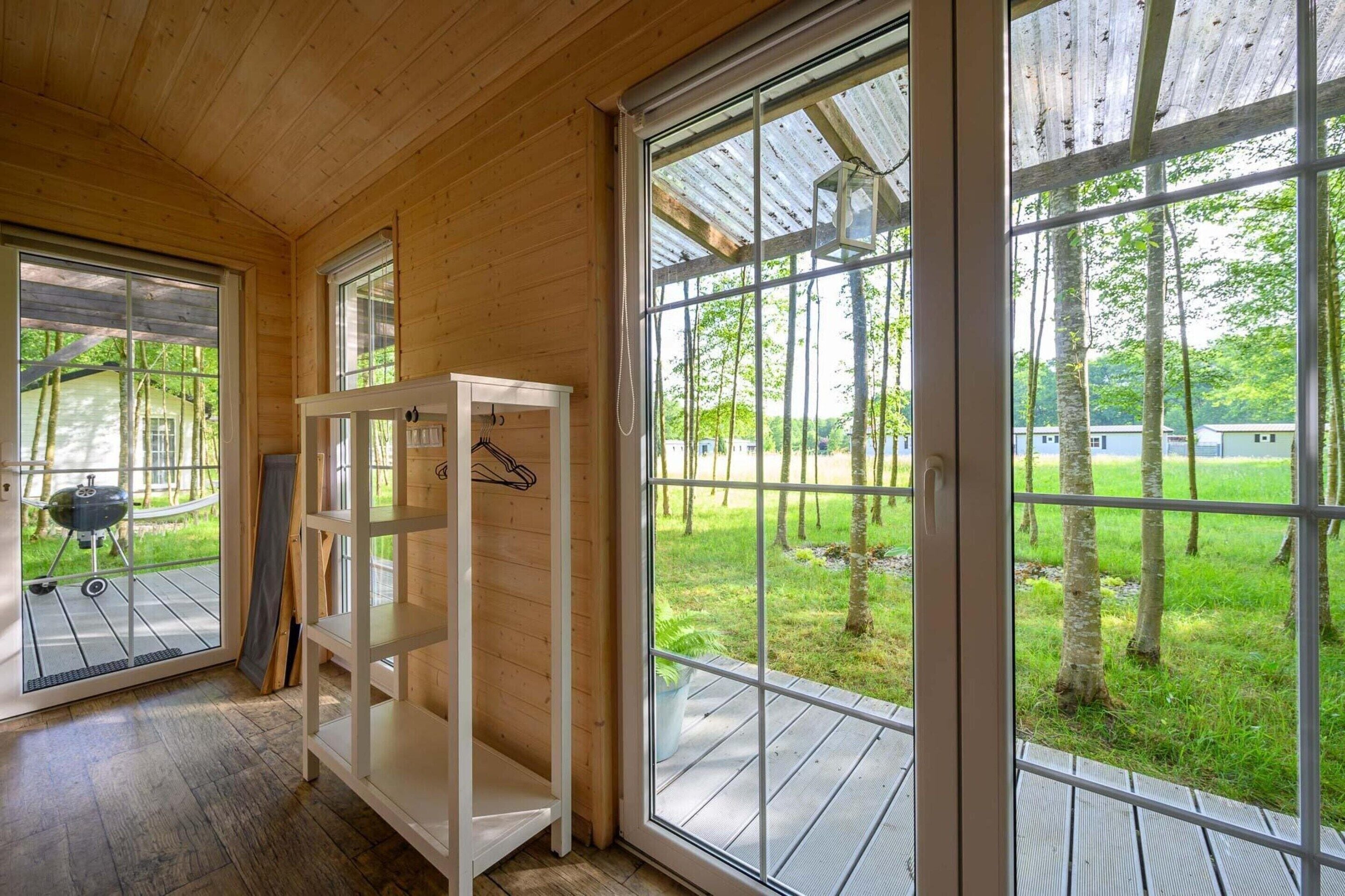 Interior de madera con amplios ventanales, un banco de madera y una parrilla en el exterior.