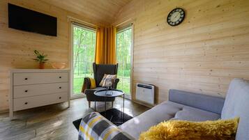 Interior moderno de una cabaña de troncos con un sofá, un sillón, una mesita, un televisor y un reloj en la pared.