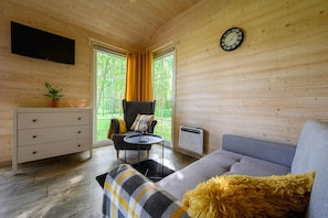 A modern log cabin interior with a sofa, a chair, a small table, a television, and a clock on the wall. - Comfortable Holiday Home no. 3B With a Fireplace (Darlowo)