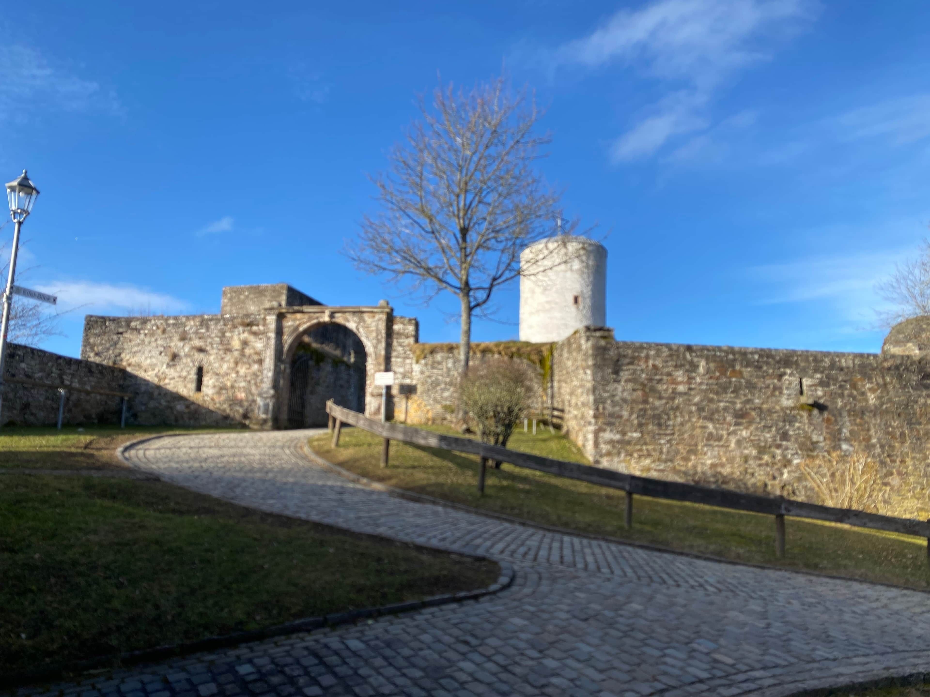 A stone pathway leading to a historic building with an arched entrance and a cylindrical tower.