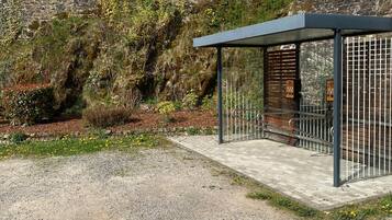 A covered outdoor seating area with a metal railing, a stone wall in the background, and a gravel ground.