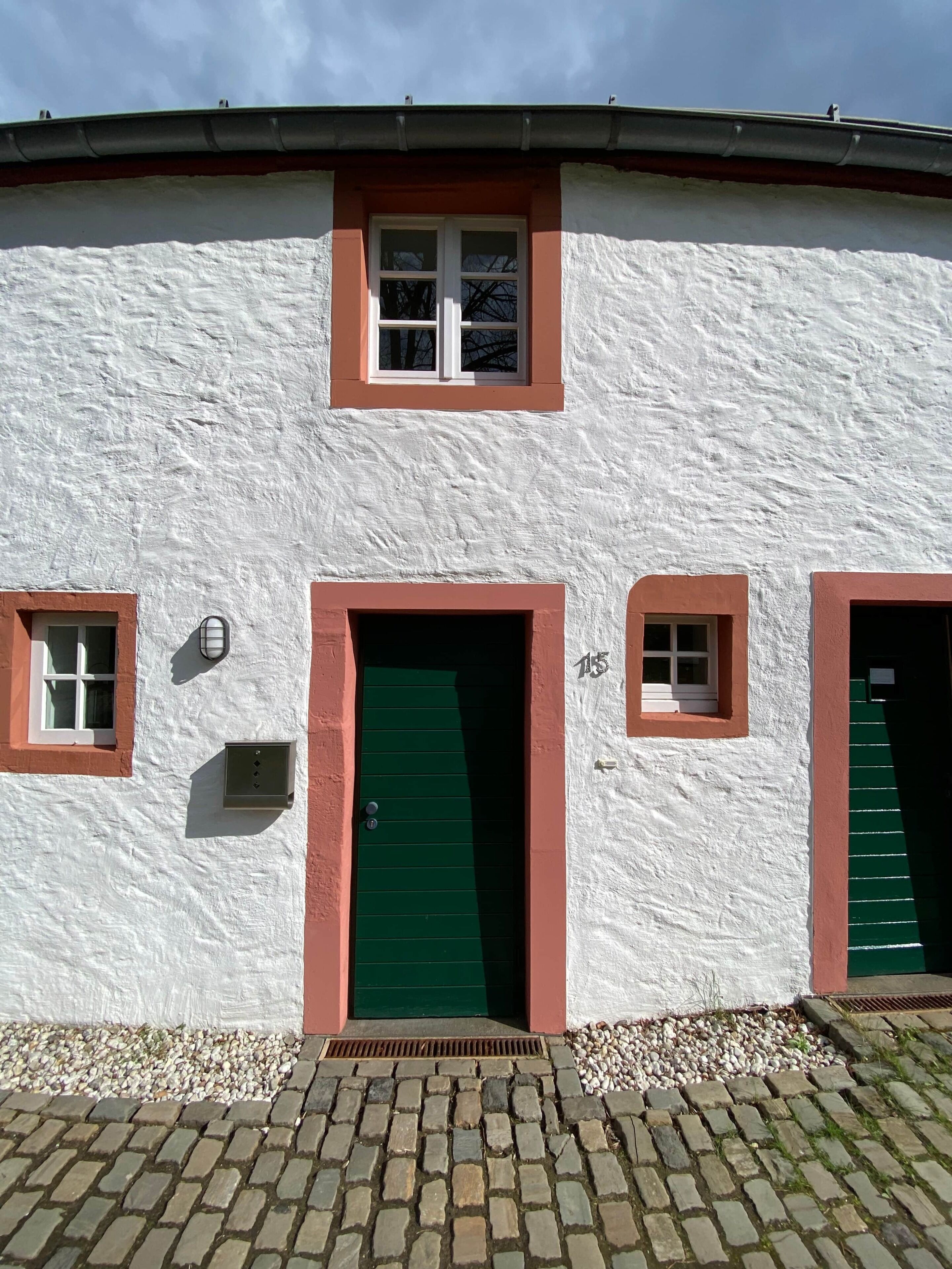 Un bâtiment à l’extérieur blanc, avec une porte verte et des fenêtres à cadre rouge.
