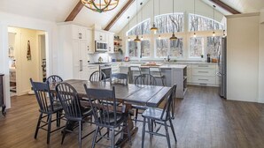 A spacious kitchen with a large island, white cabinetry, and a high ceiling with exposed beams.