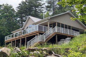 Ein zweistöckiges Haus mit Balkon, Holzterrasse und einer Treppe, die zu der oberen Etage führt.