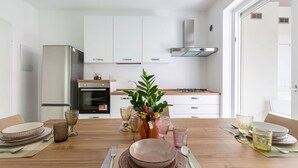 Une cuisine moderne avec des meubles blancs, un réfrigérateur en acier inoxydable et un îlot central agrémenté d’un vase de fleurs.
