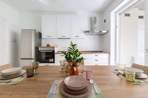A modern kitchen with white cabinets, a stainless steel refrigerator, and a central island with a vase of flowers. - Dimora Melograno by BarbarHouse (Lecce)