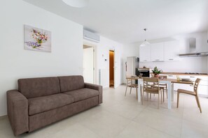 A modern living room with a brown sofa, a dining area with a table and chairs, and a kitchen with white cabinets and a stainless steel refrigerator. - Dimora Melograno by BarbarHouse (Lecce)