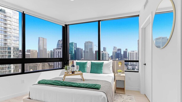 Ein modernes Schlafzimmer mit einem großen Bett, einem Nachttisch, einem Beistelltisch, einem Spiegel und Blick auf die Stadt.
