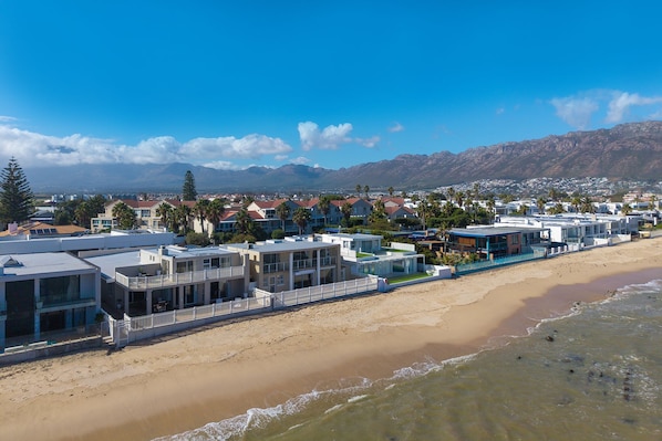 A coastal hotel with multiple buildings, a beach, and mountains in the background.