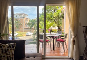 Ein Zimmer mit einer Schiebeglastür, die auf einen Balkon mit Tisch und Stühlen, einem Sofa und einer Topfpflanze führt.