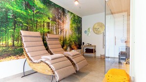 Una habitación con dos sillones reclinables, un gran mural de un bosque, un reloj de pared redondo y una pequeña mesa de madera con una cesta.