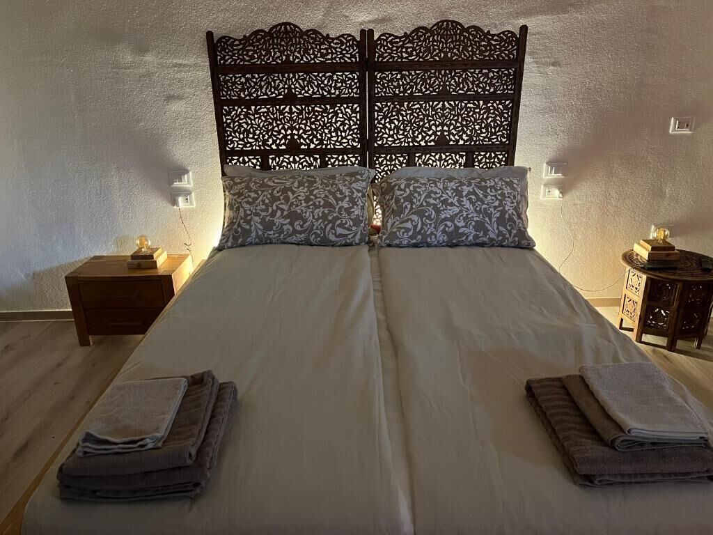 Un lit double agrémenté d’une tête de lit décorative, deux tables de chevet avec des lampes et des serviettes pliées posées sur le lit.