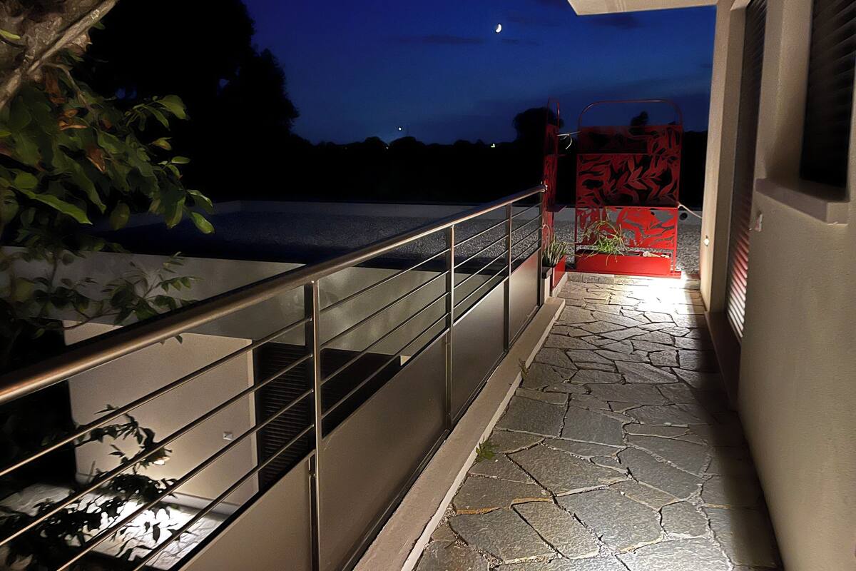 A nighttime view of a building's exterior with a metal railing, stone steps, and a red gate.