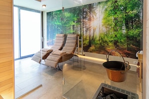 A modern room with a glass wall, two reclining chairs, a fireplace, and a forest mural.