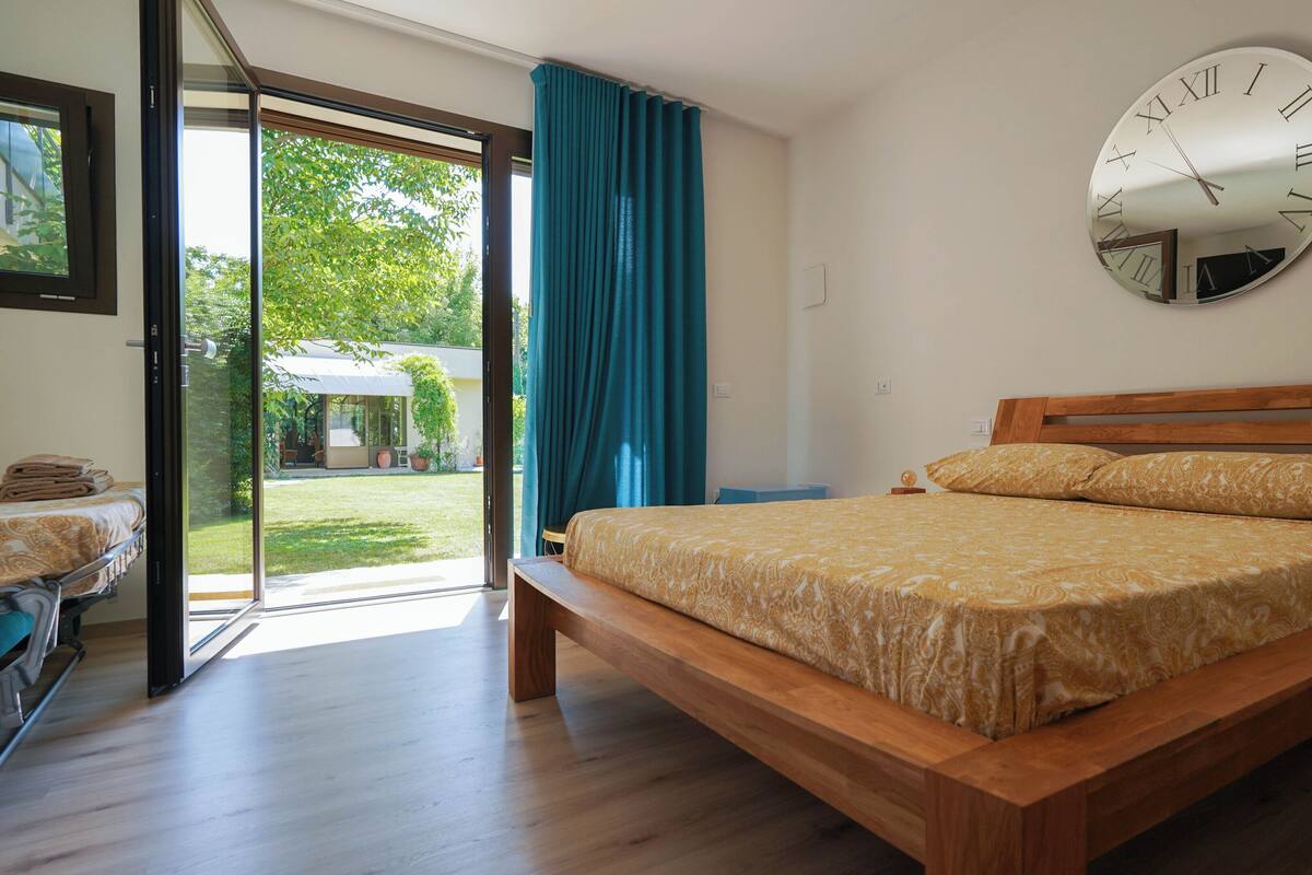 A bedroom with a wooden bed, a large wall clock, and a sliding glass door leading to a garden.