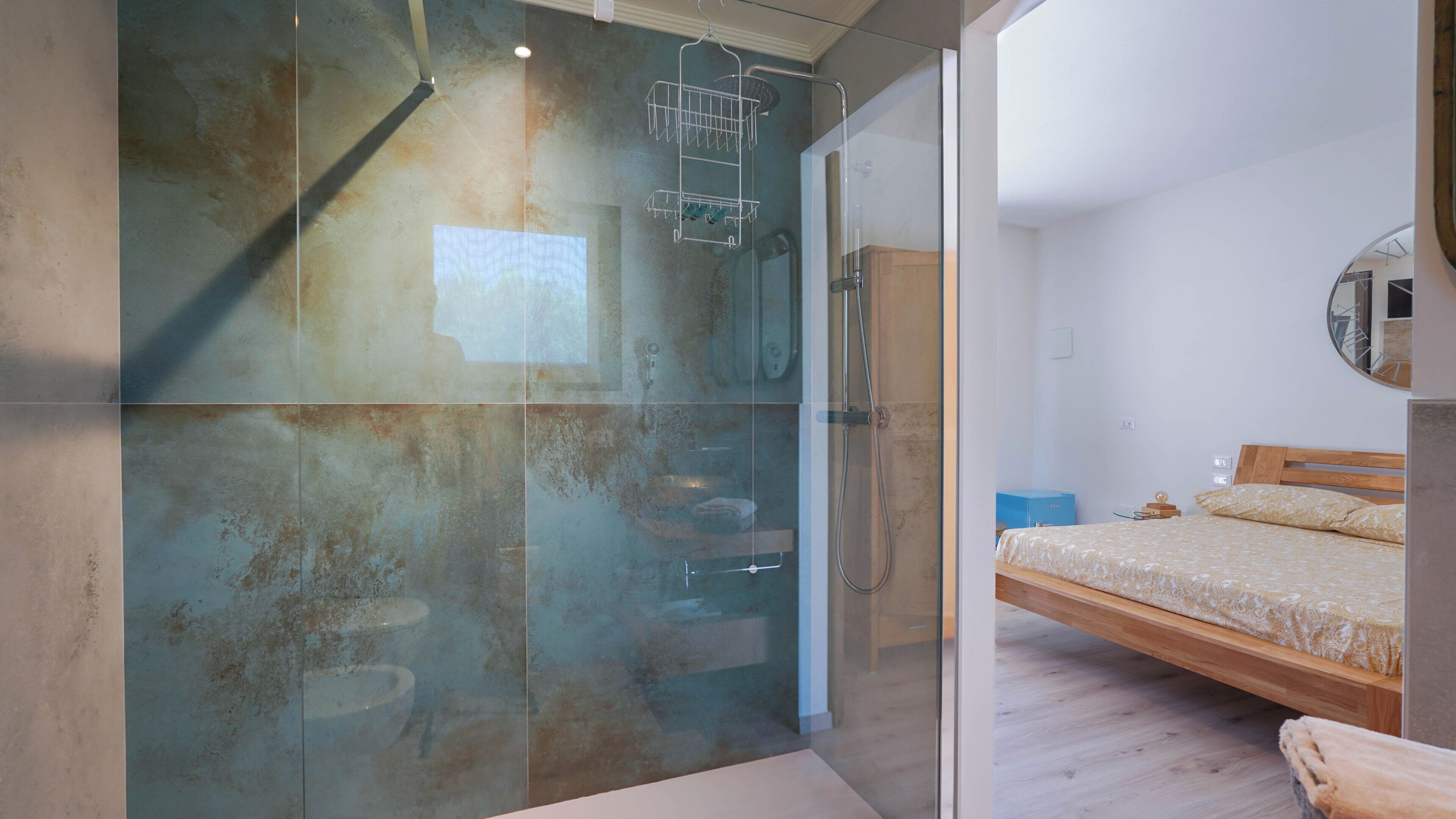 Un dormitorio moderno con cabina de ducha de vidrio, cama de madera y un espejo en la pared.