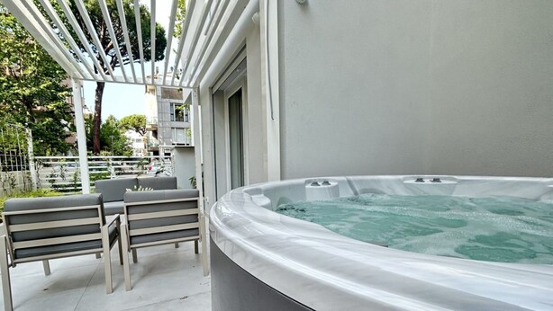 Ein Whirlpoolbereich mit einer Pergola, zwei grauen Bänken und Blick auf die umliegenden Gebäude.