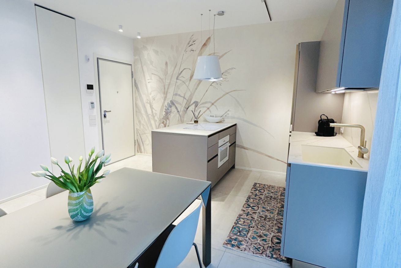 A modern kitchen with a dining table, a vase of flowers, and a patterned rug.