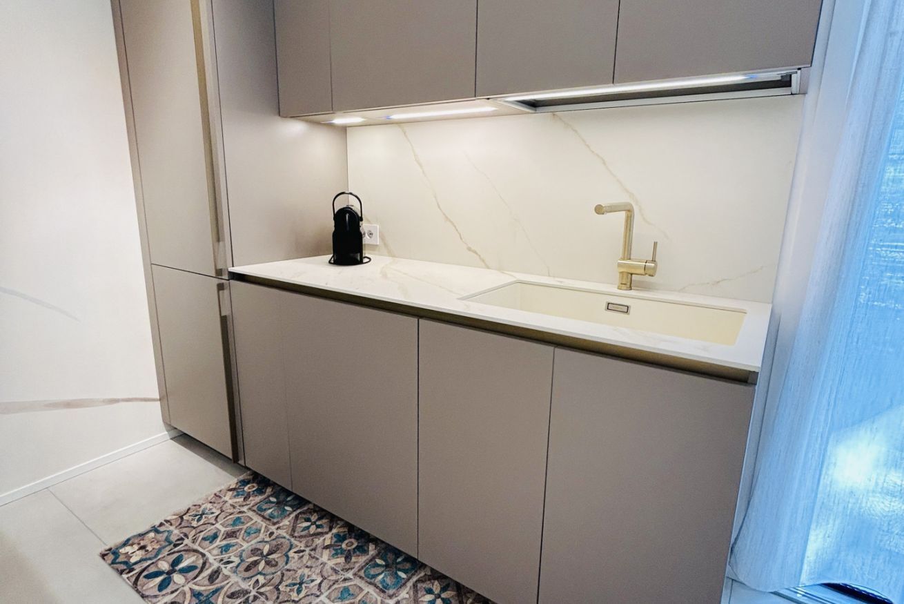 A modern kitchen with a white countertop, a sink, and a kettle.