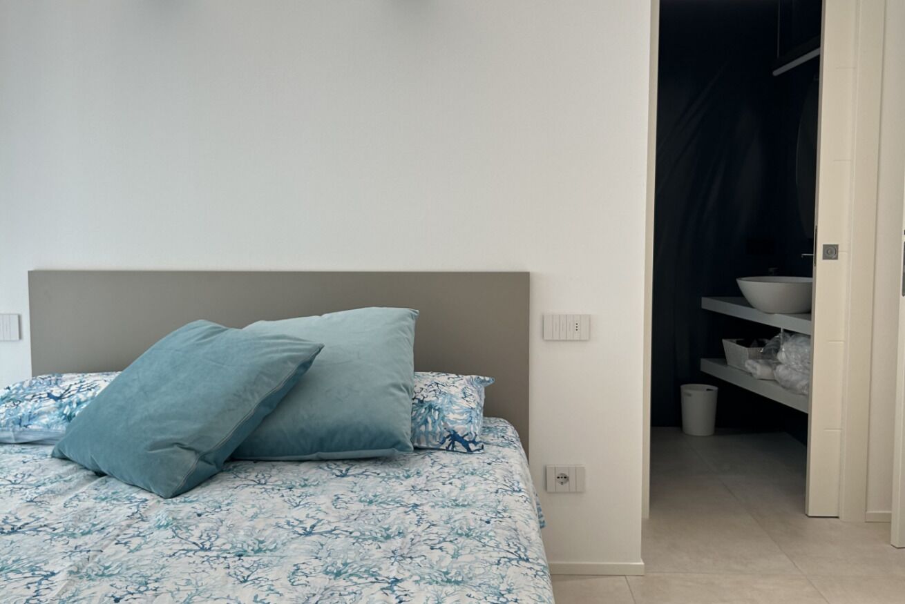 Un dormitorio con una cama, dos almohadas, una mesita de noche y un armario con estantes.