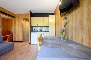 A modern kitchen with wooden cabinets, a dining table with placemats, and a small table with flowers. - Single-story Holiday Home by the Pond no. 1 (Darlowo)