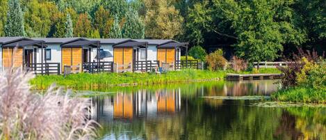 A row of cabins with a pond in the foreground, surrounded by lush greenery.