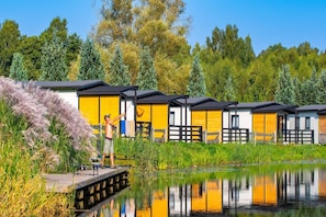 A row of yellow cabins with a dock extending into a calm body of water, surrounded by lush greenery and trees. - Single-story Holiday Home by the Pond no. 5 (Darlowo)