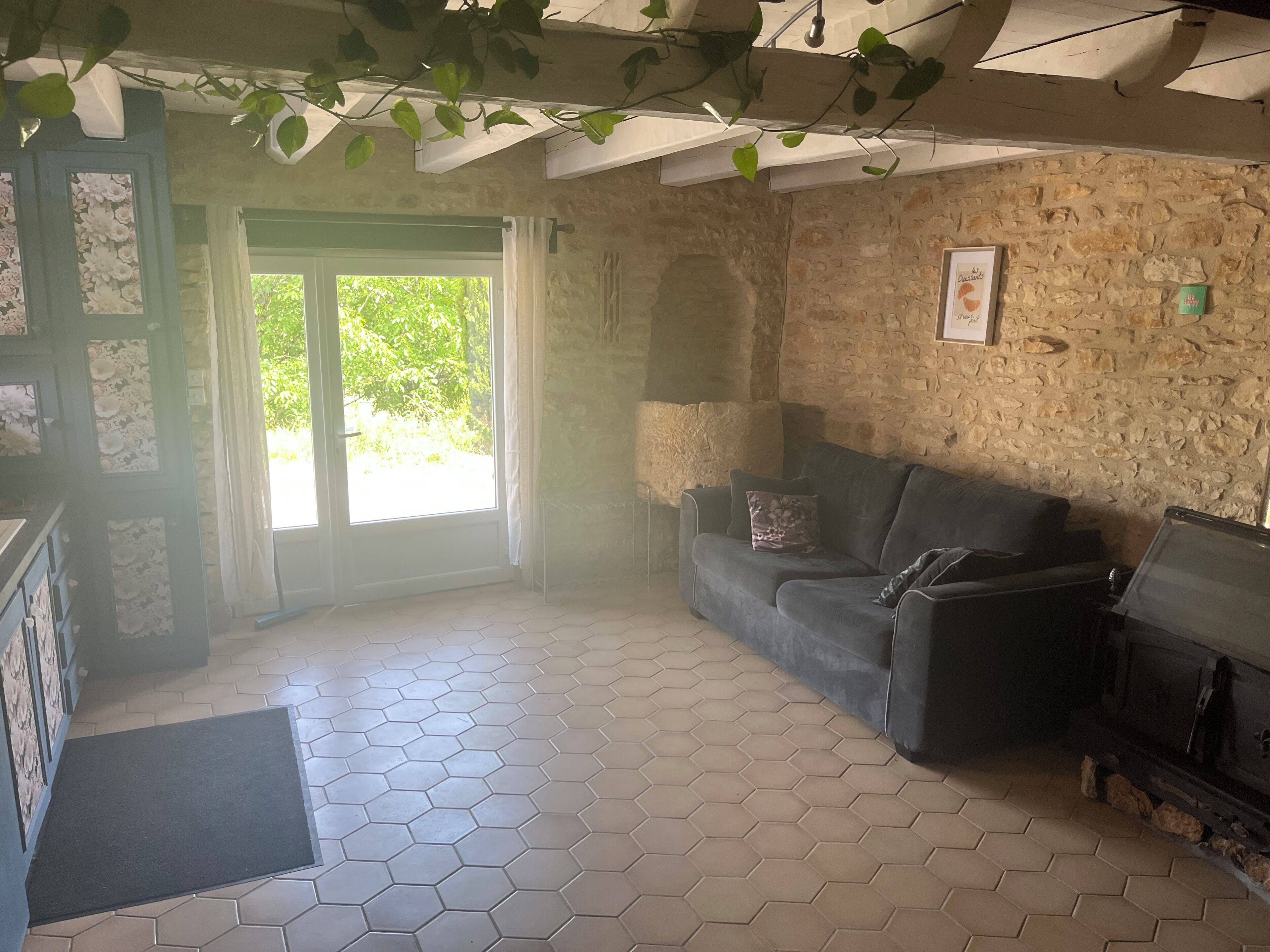 Une pièce avec un mur en pierre, un canapé, une cheminée et une porte donnant sur un paysage verdoyant.