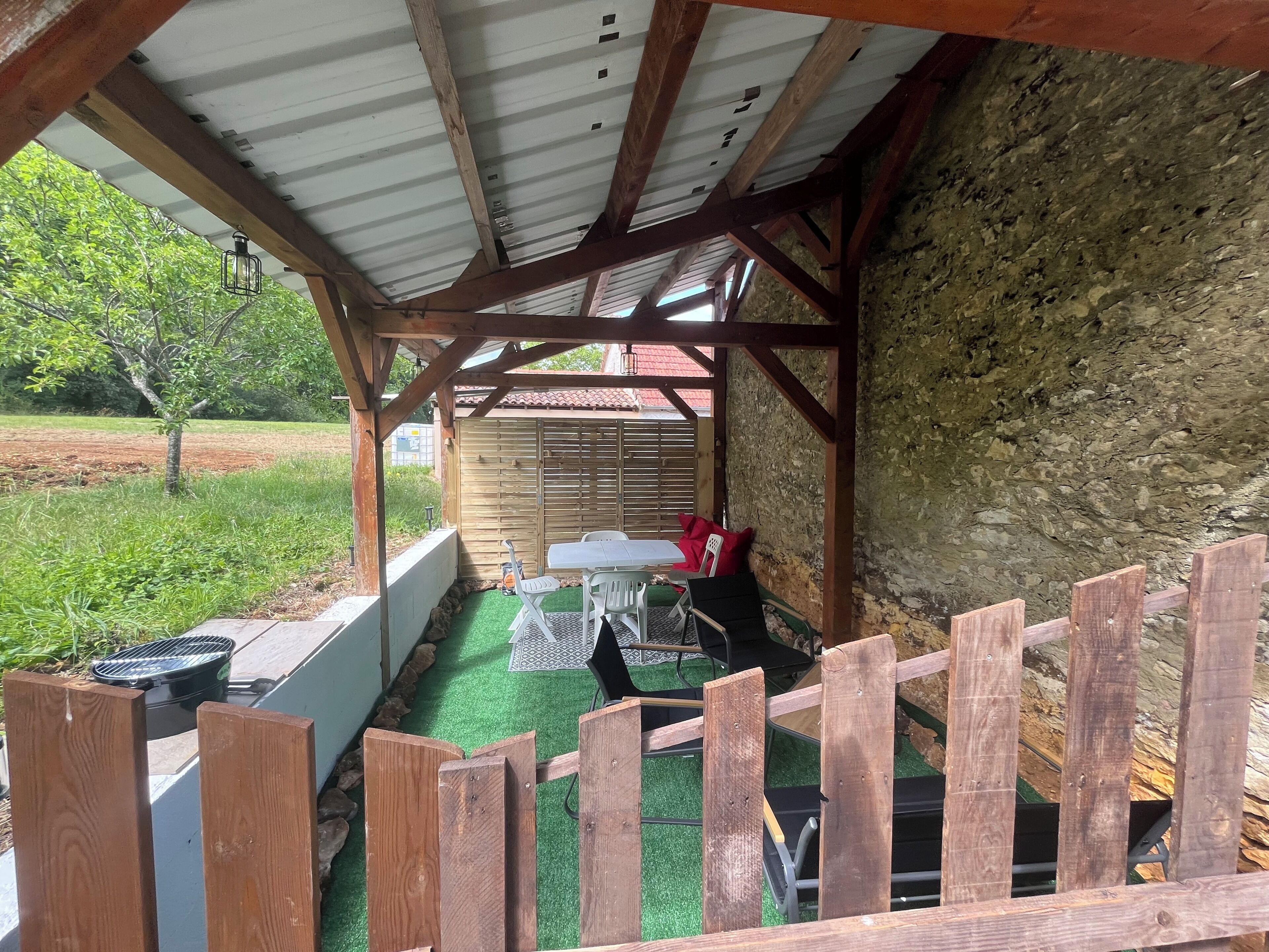 Un espace extérieur abrité, doté d’une clôture en bois, d’une table, de chaises et d’un barbecue.