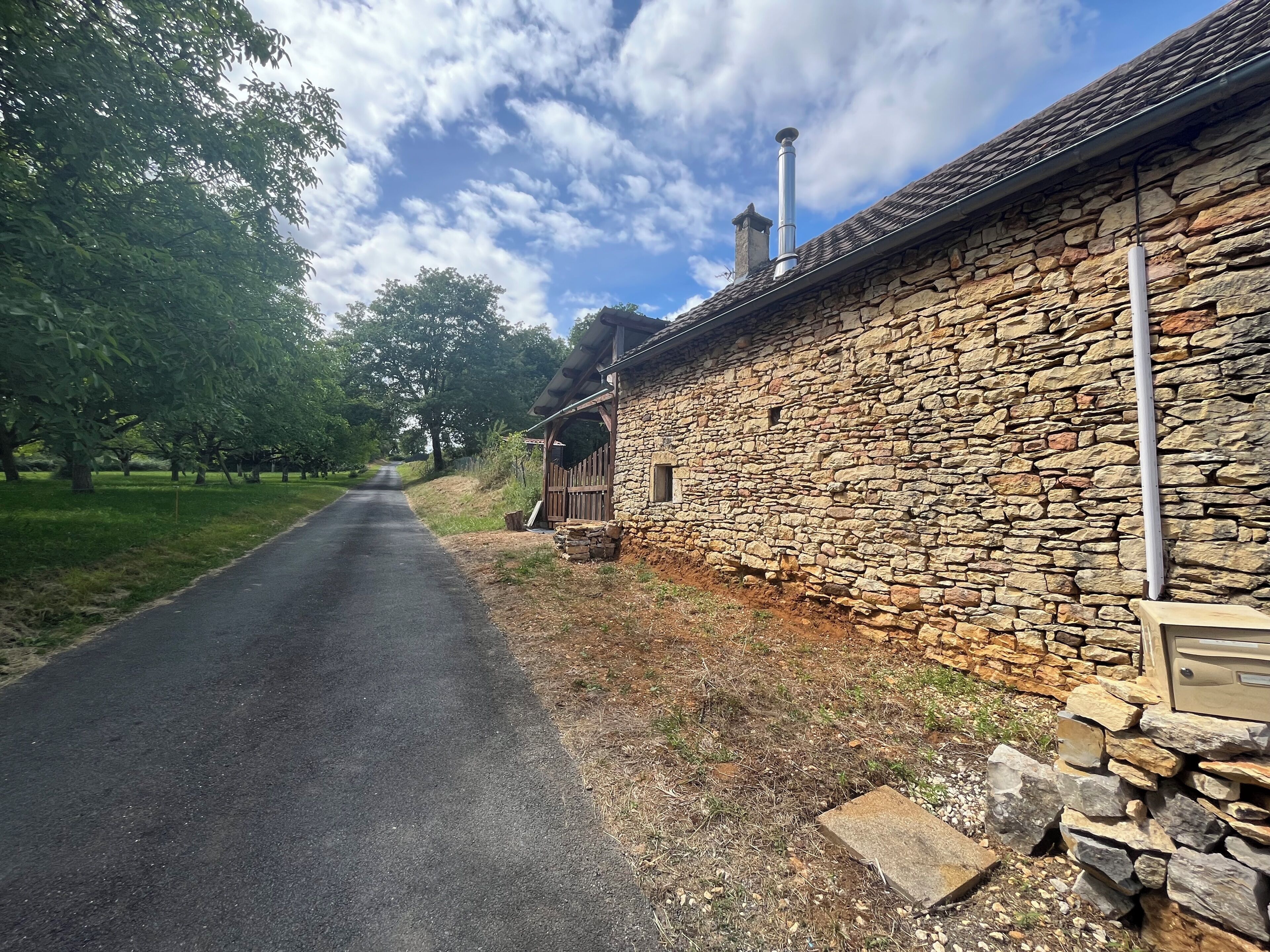 Ein Steinhaus mit Holztür, Schornstein und einer gepflasterten Straße, die sich fortsetzt.
