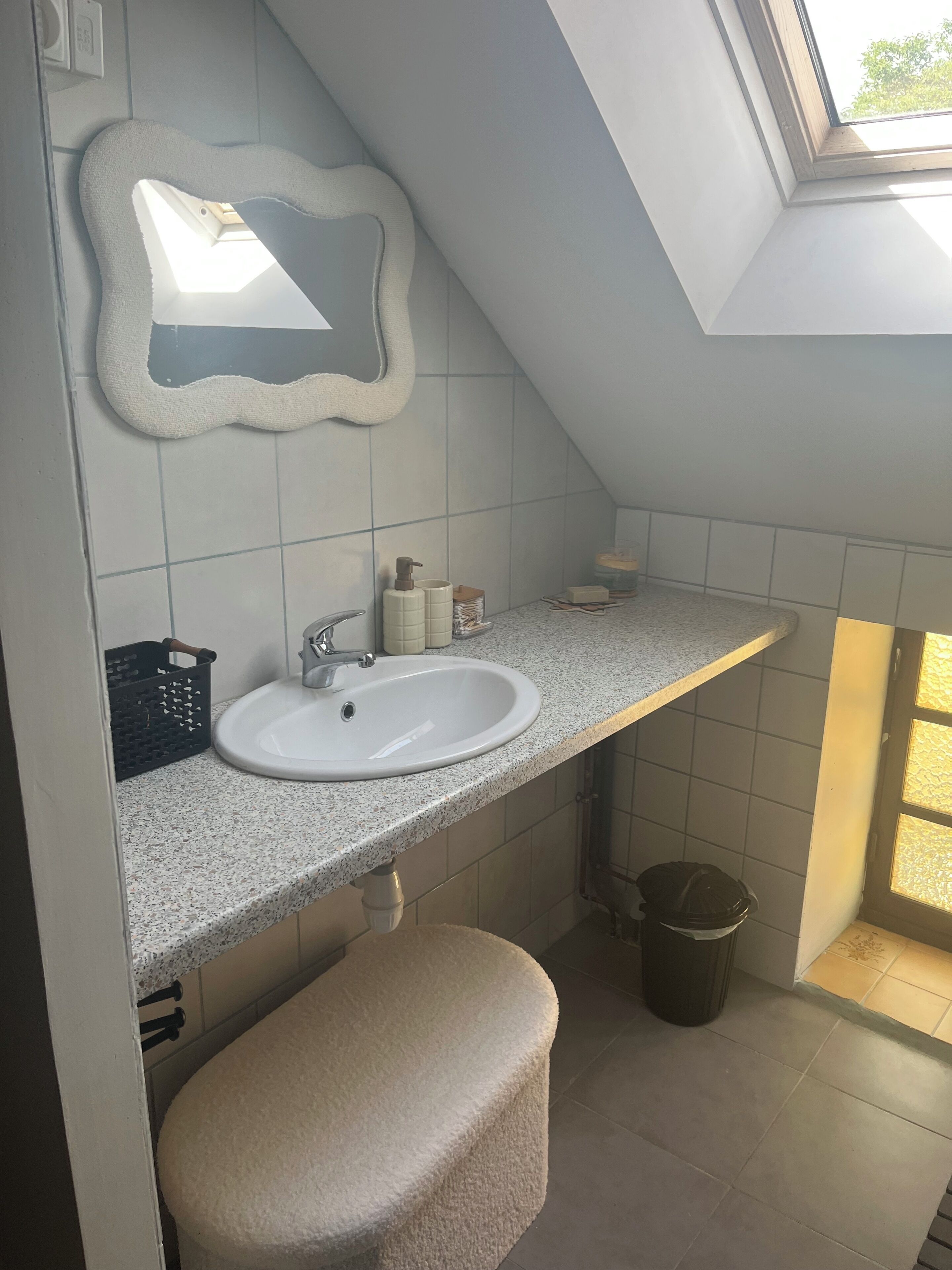 Un baño con tragaluz, un lavabo blanco, un espejo y un perchero para toallas.