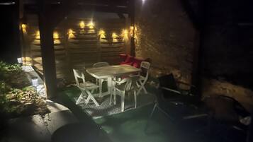 An outdoor patio area with a table and chairs, surrounded by stone walls and illuminated by string lights.