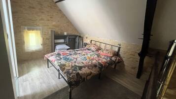 A bedroom with a sloped ceiling, a bed with floral bedding, a wardrobe, and a small window.