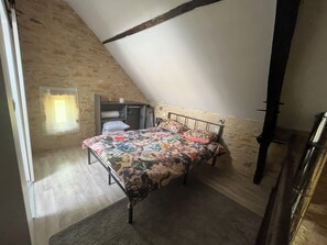 Una camera da letto con soffitto spiovente, un letto con lenzuola a fiori, un armadio e una piccola finestra.