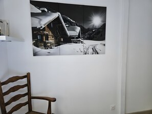 Una stanza con una sedia di legno, un quadro appeso al muro raffigurante una montagna innevata e una parete bianca.