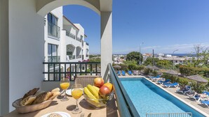 Ein Balkon mit Frühstückstisch, ein Swimmingpool und Blick auf ein weißes Gebäude mit Balkonen.