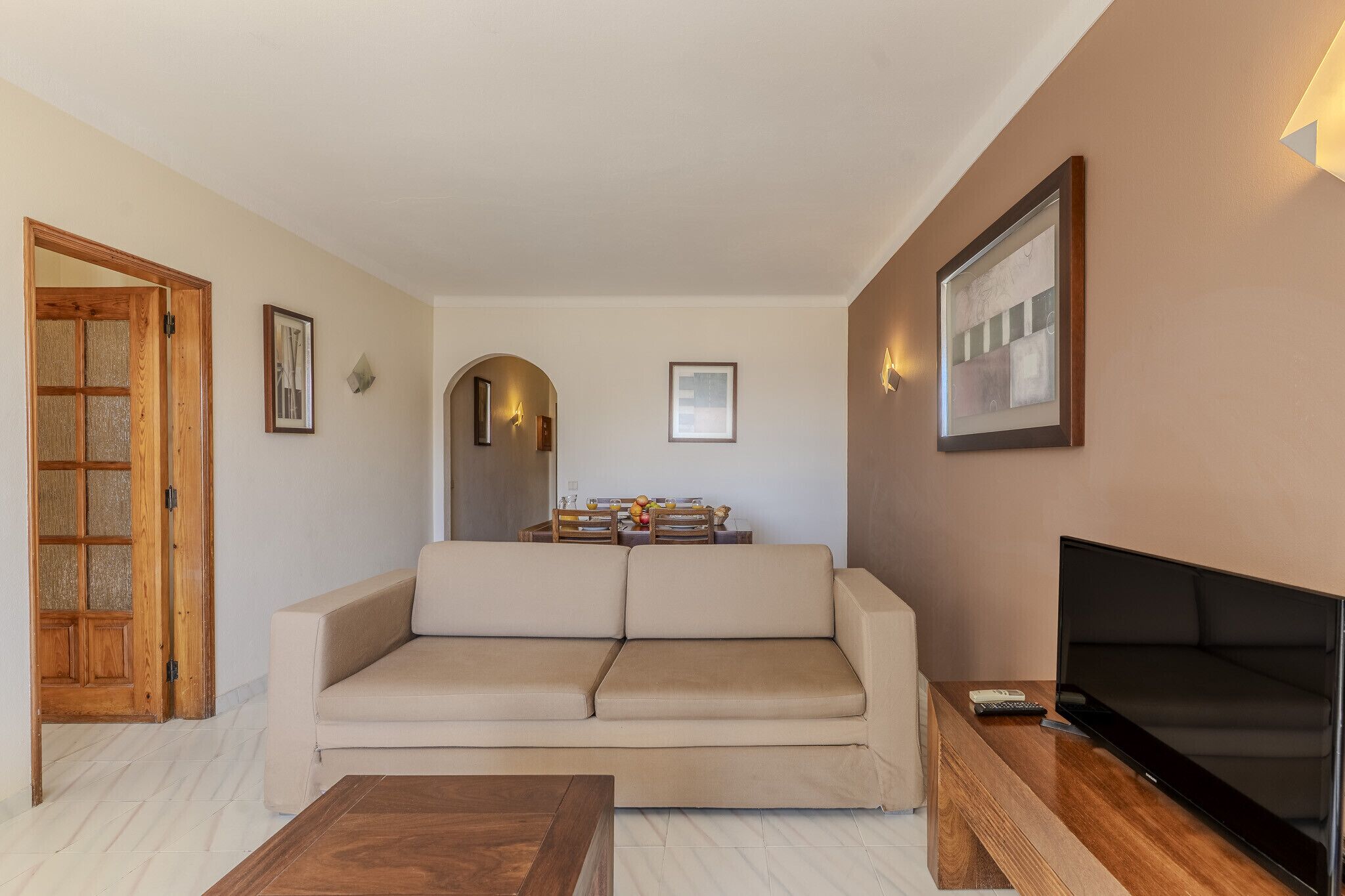 A living room with a sofa, a coffee table, a TV, and a wooden door.