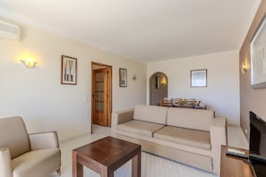 A living room with a sofa, a coffee table, and a TV. There are framed pictures on the walls and a door with glass panels. - #384 Bright Pool View Apartment | AC & Balcony (Albufeira)