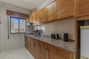A kitchen with wooden cabinets, a granite countertop, a built-in oven, a coffee maker, a toaster, and a kettle. - #384 Bright Pool View Apartment | AC & Balcony (Albufeira)