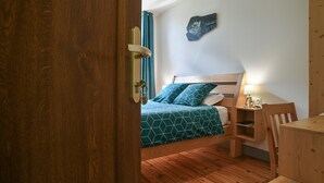 A room with a wooden floor, a bed with a geometric-patterned bedspread, a bedside table with a lamp, and a wall-mounted artwork. - La Chartreuse Guest Room with Shared Garden and Wi-Fi (Saint-Franc)