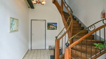 Un escalier en bois avec une rampe en métal, une porte ornée d’un tableau et un lustre.