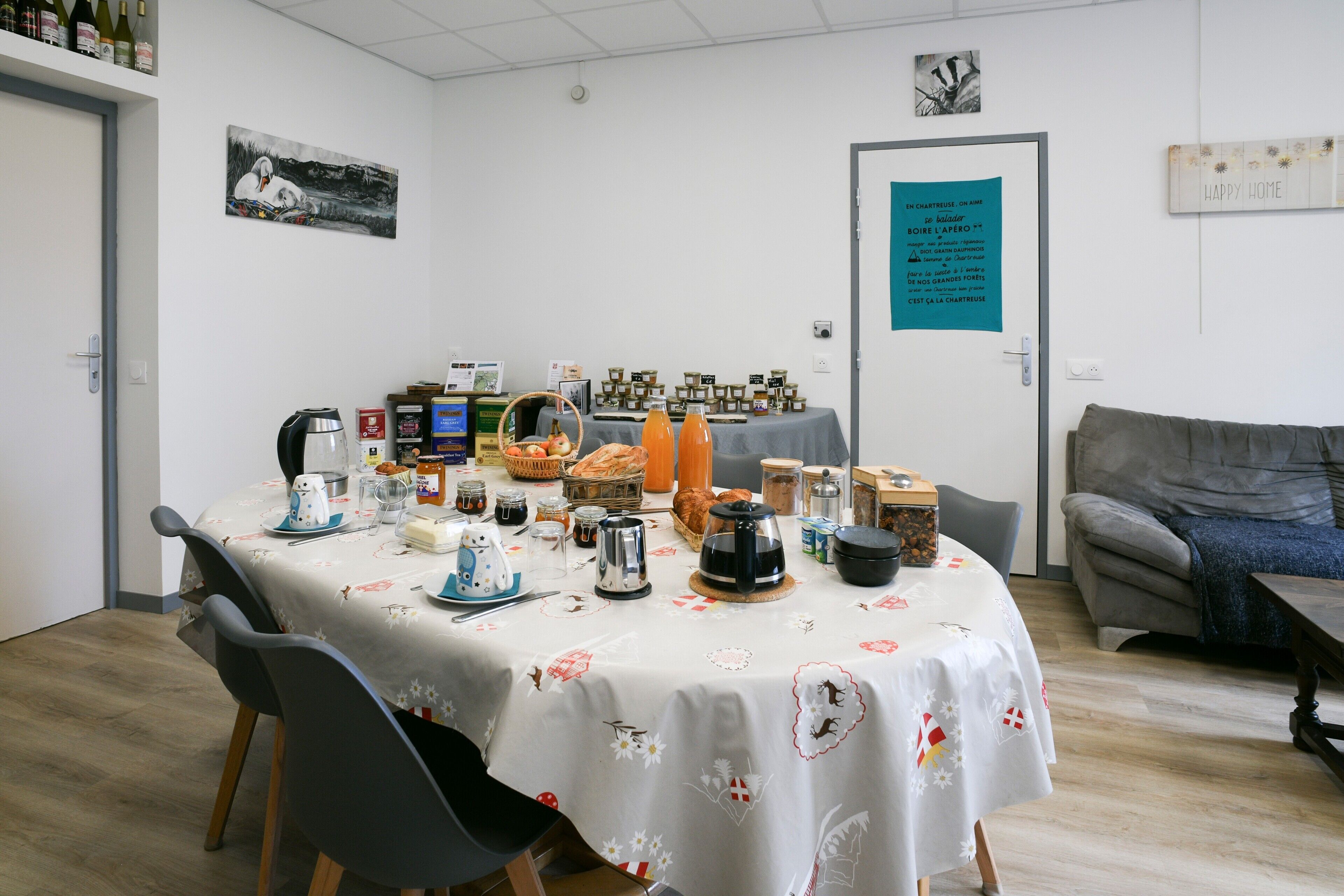 A dining area with a table set for four, surrounded by chairs. There are various food items and condiments on the table.