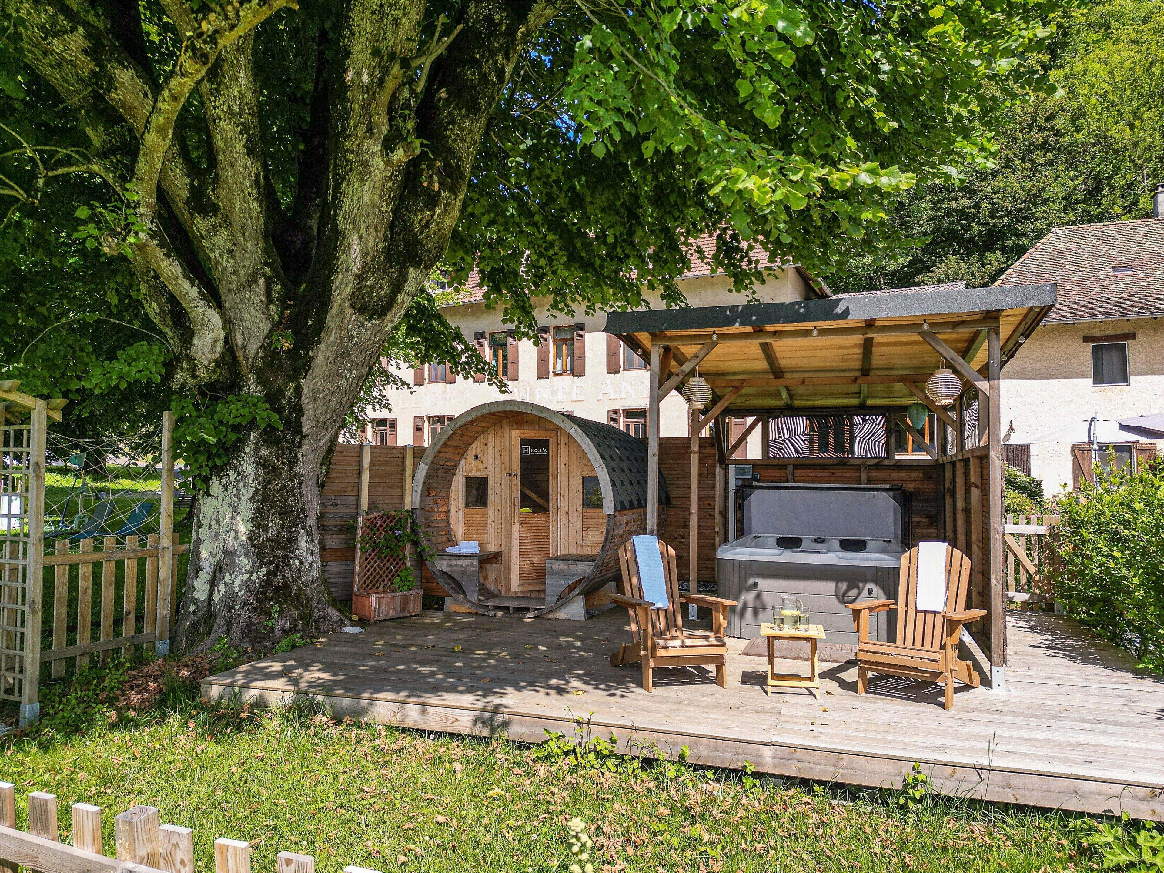 Une terrasse en bois avec des sièges d’extérieur, un jacuzzi et une structure en bois dotée d’une porte.